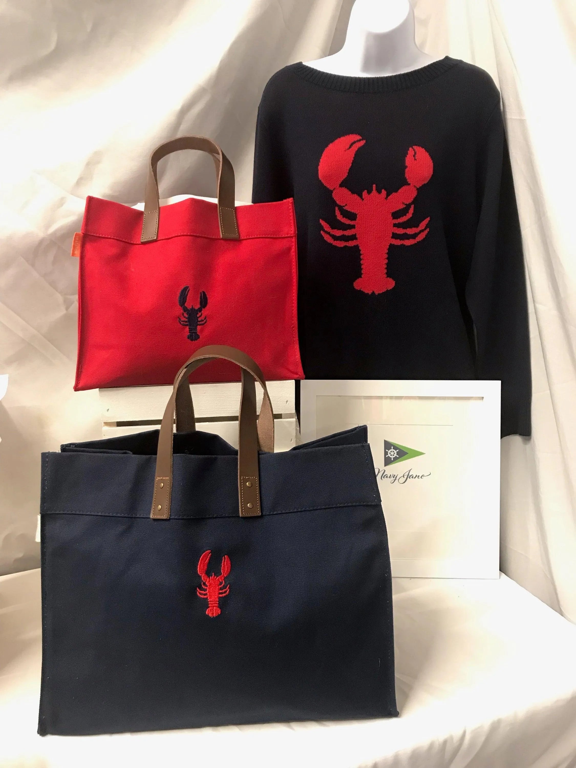 picture of a navy sweater and red lobster on it.  Small red tote with navy lobster.  Leather handle in brown .  Large version is navy with red lobster.  